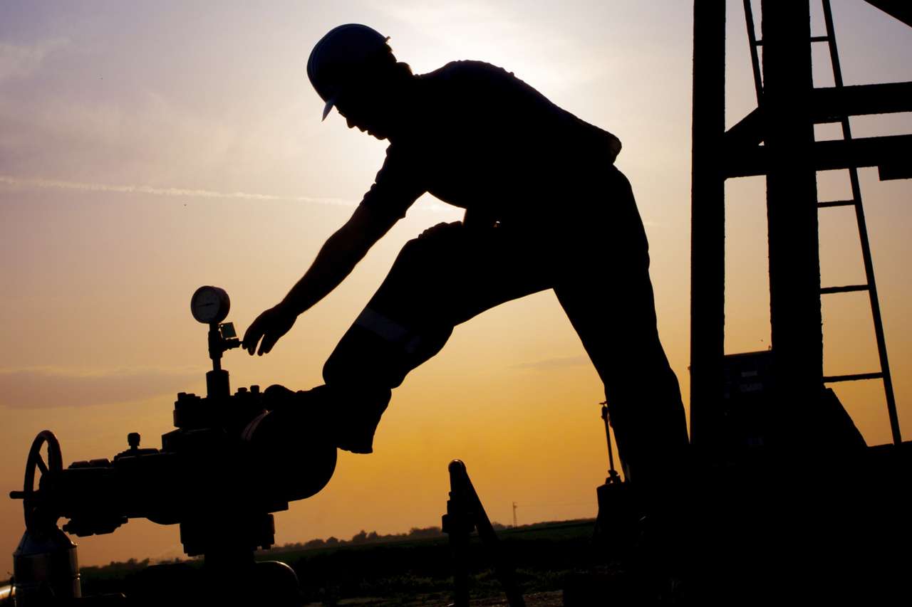 Engineer operating a wellhead valve at sunset